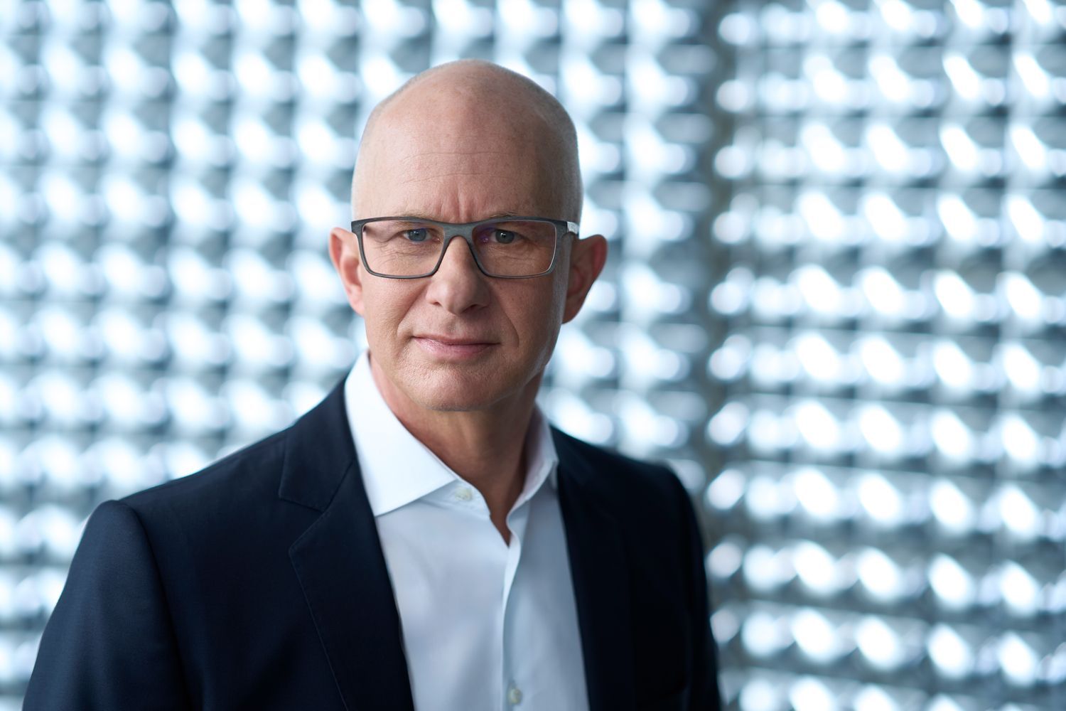 Mann im Anzug und Brille vor metallischer Wand